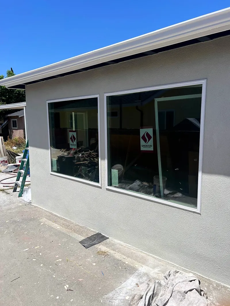 Freshly stuccoed addition with two large new windows, construction sticker still on the glass