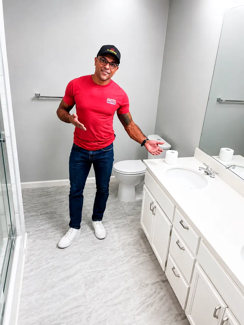 Junior Prata, owner of Junior Elite Services, standing in a finished bathroom with a white vanity, gray tile floor and glass shower