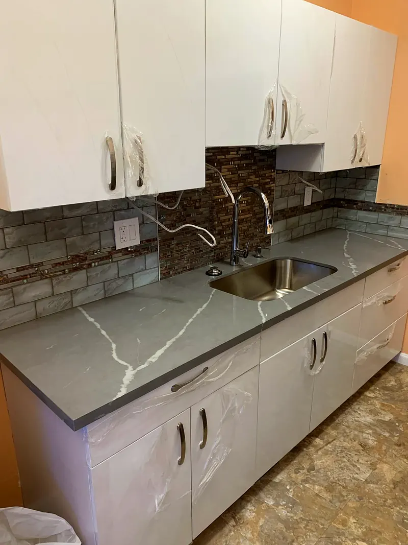 New white gloss cabinets still in protective film, gray quartz counter and a glass mosaic backsplash