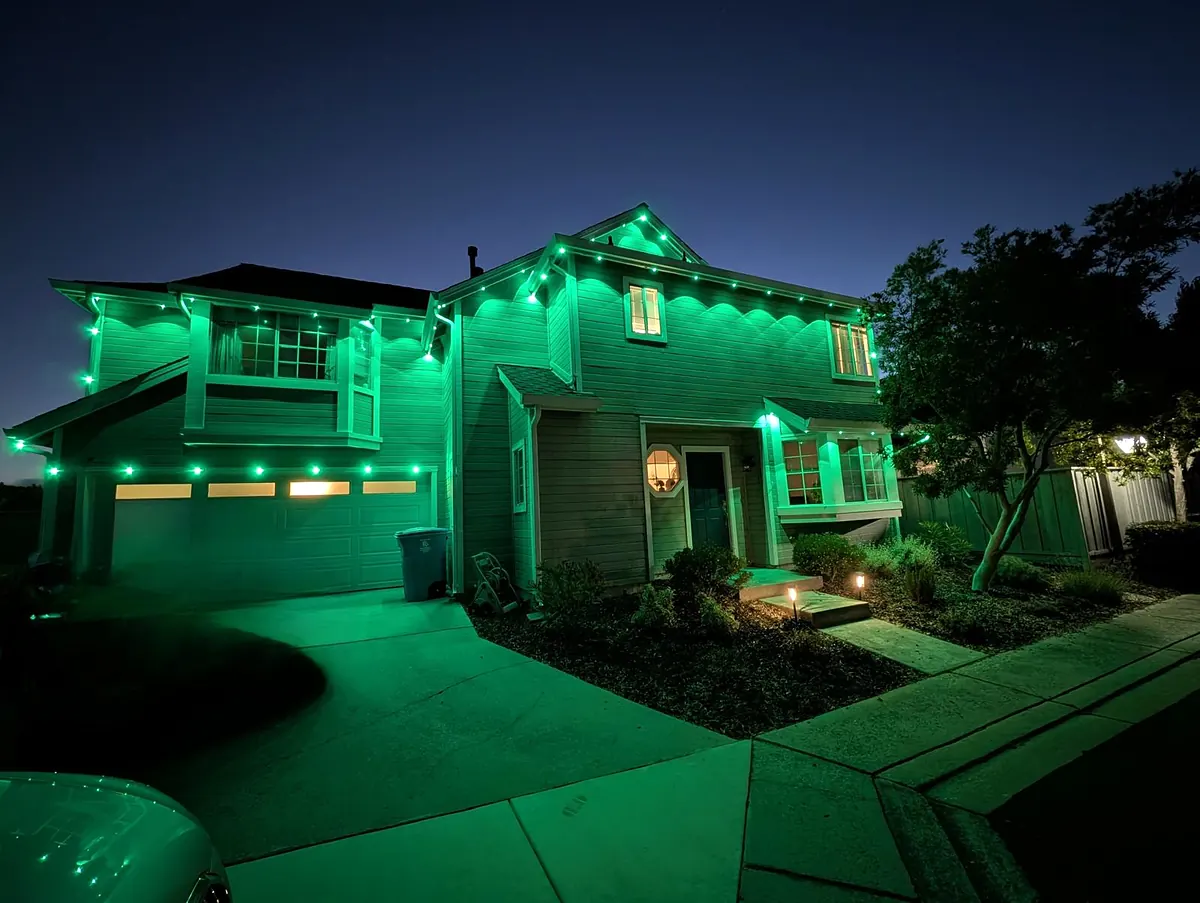 Two story house with green lights along the rooflines and porch at dusk