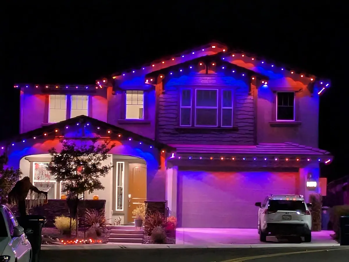Two story craftsman house with purple and red lights outlining the gables and porch at night