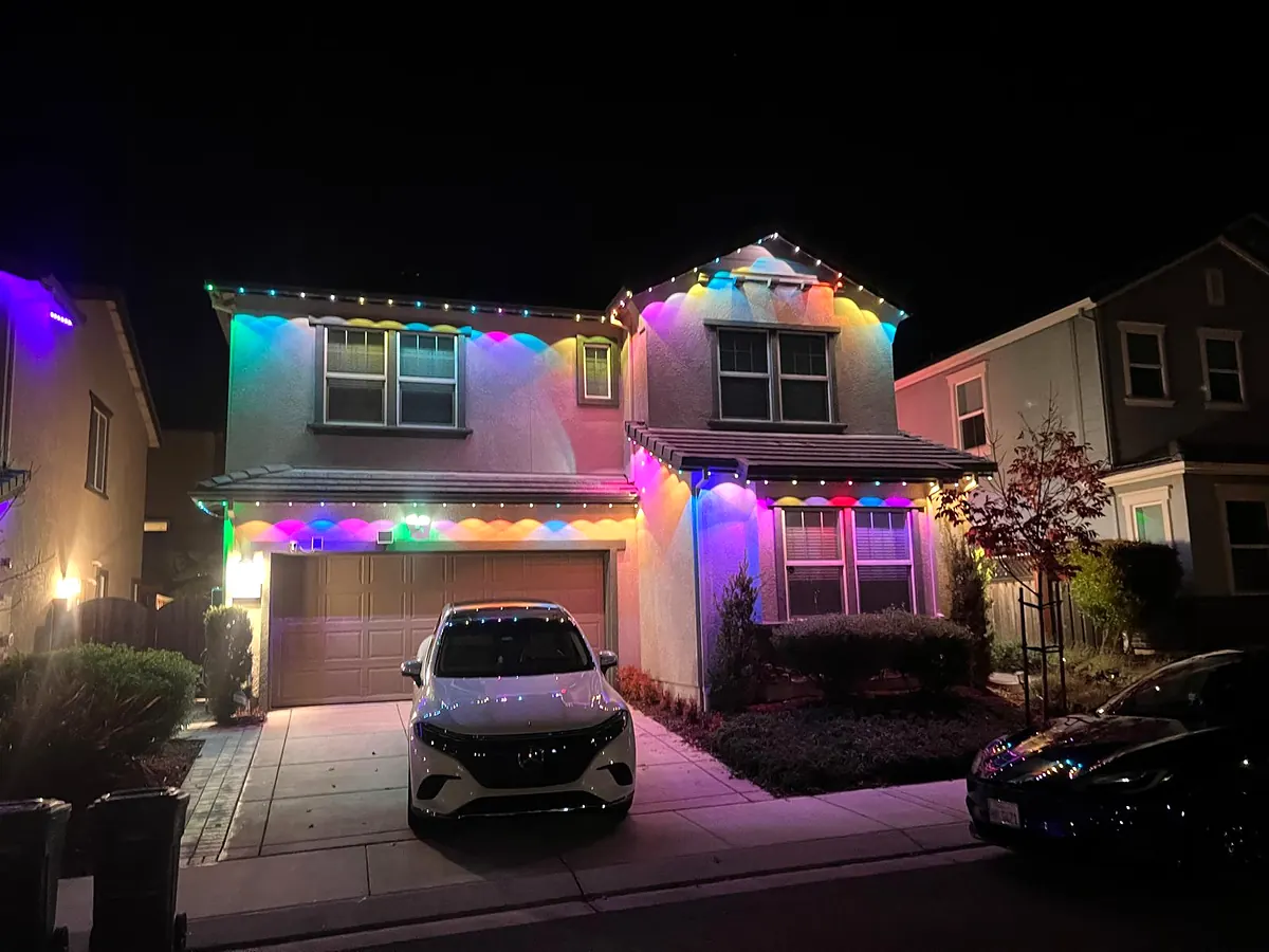Two story house with color LED lights along every roofline and the garage eave at night