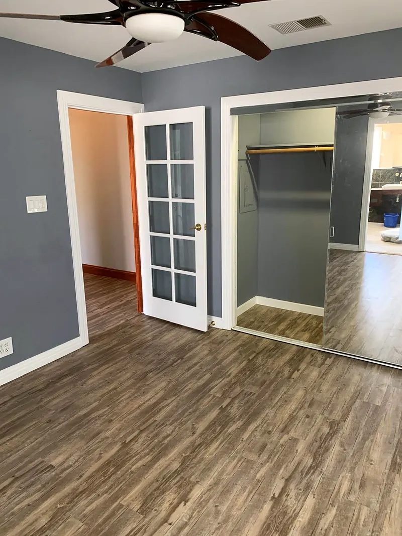 Gray bedroom with a white French door, mirrored closet doors and new plank flooring