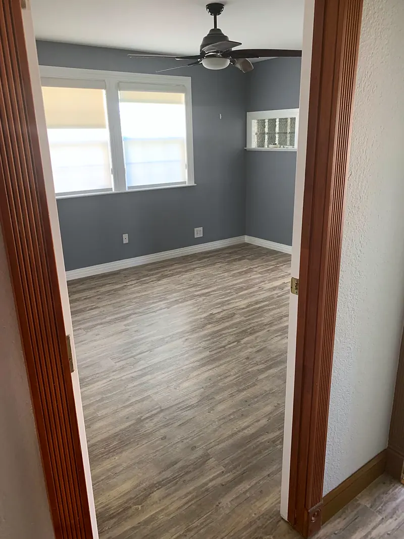 Bedroom painted gray with bright white baseboards and new wood-look plank floor