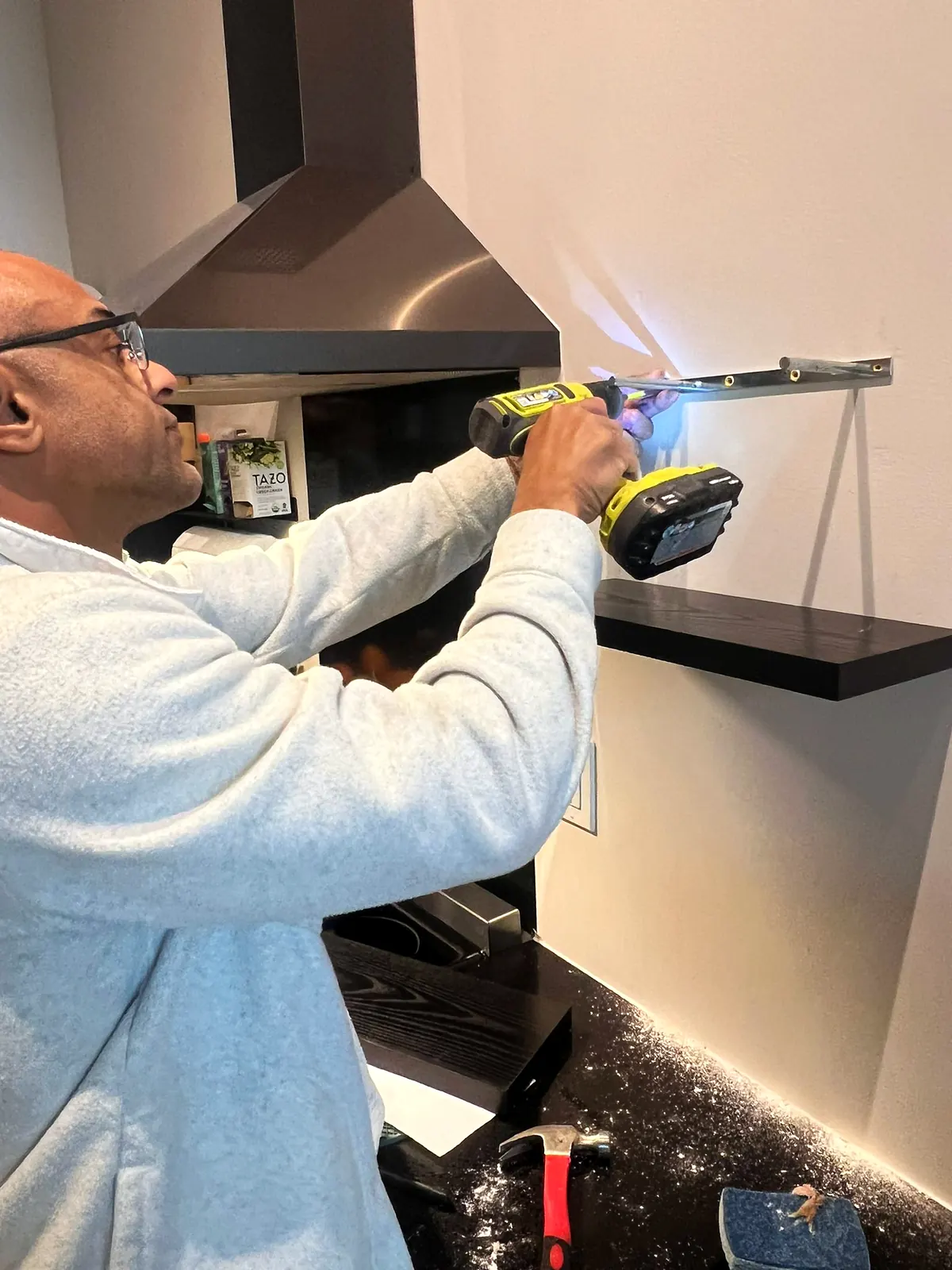 Floating shelf bracket being drilled into a kitchen wall next to a range hood