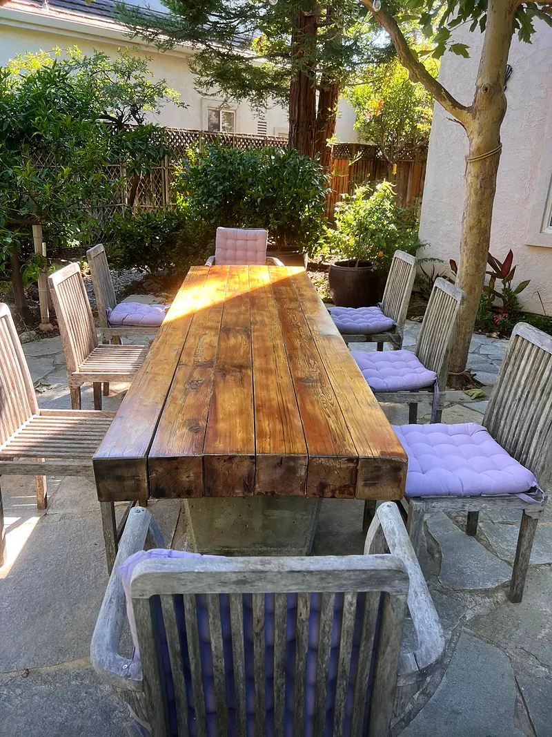 Heavy timber dining table refinished on a stone patio with chairs around it
