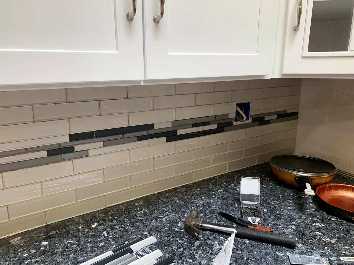 Subway tile backsplash with a glass accent strip, tools and a level on the granite counter