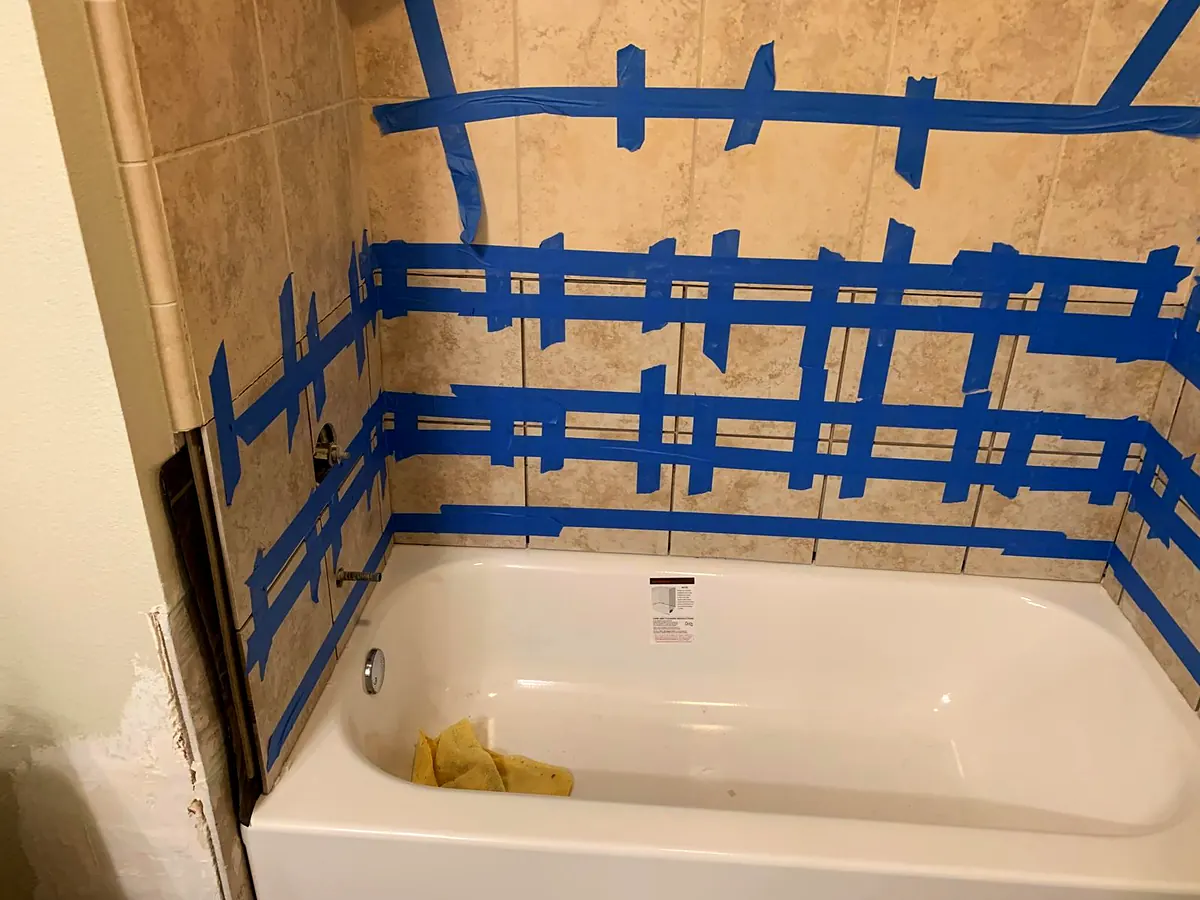 New bathtub with a tile surround held in place with blue tape while the adhesive sets